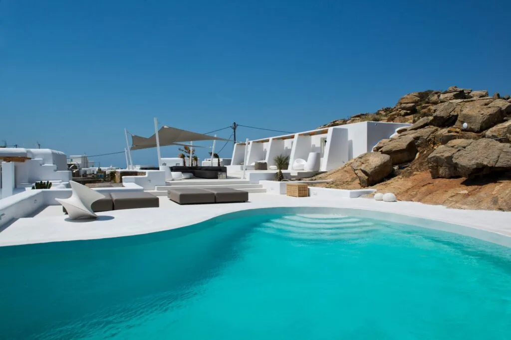 Una piscina al aire libre junto a asientos blancos y una ladera rocosa.