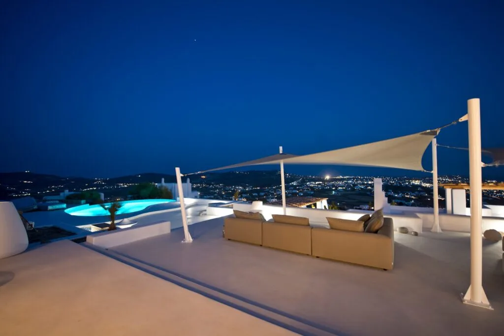 Una terraza en la azotea de noche tiene asientos bajo un toldo y vistas a las luces de la ciudad.