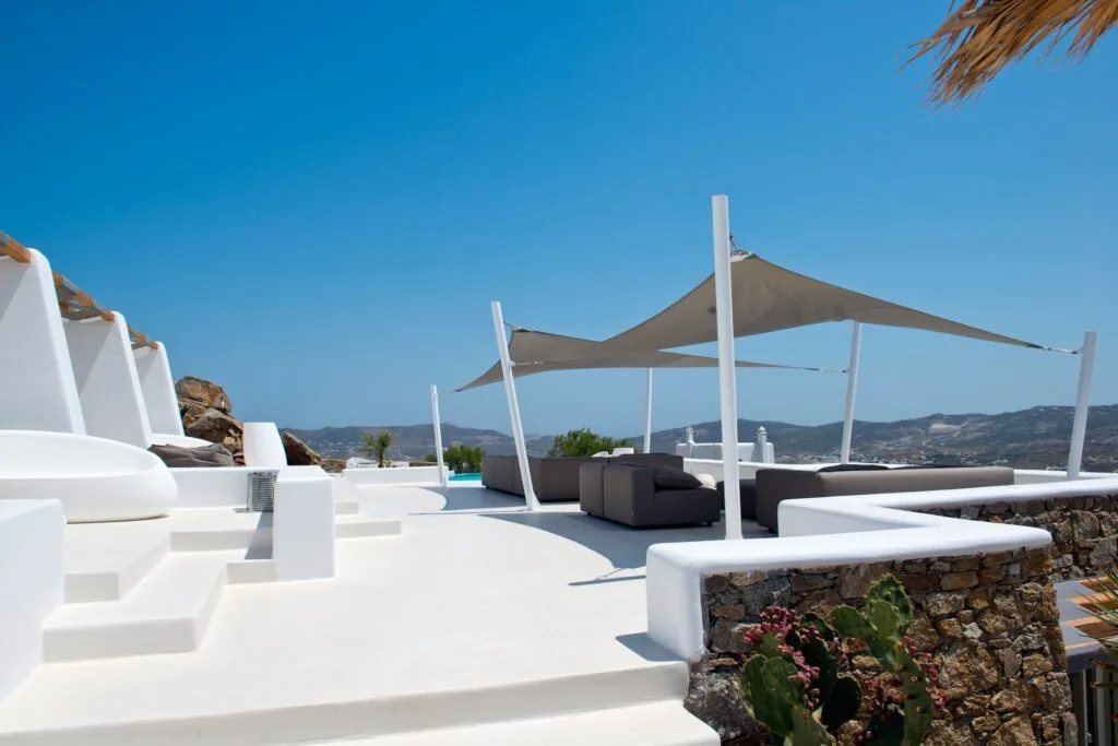 Una terraza exterior blanca con asientos a la sombra y vistas a las colinas.