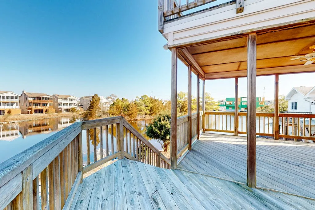 A wooden deck overlooks a calm pond and nearby homes.