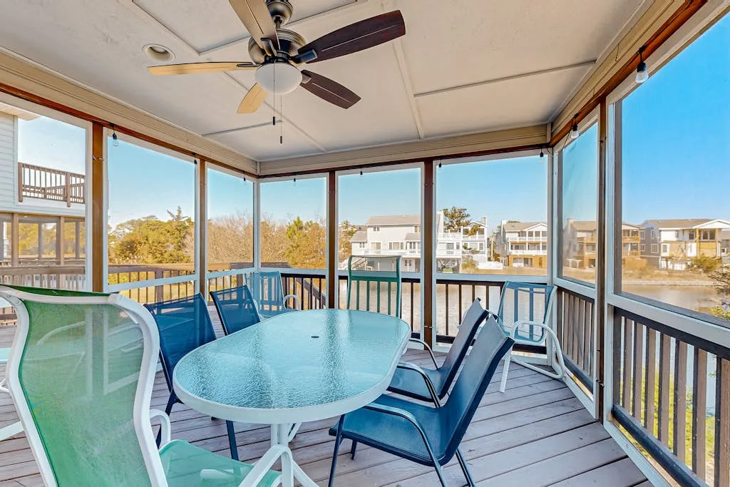 A glass-enclosed porch with a dining table and chairs overlooking nearby buildings.
