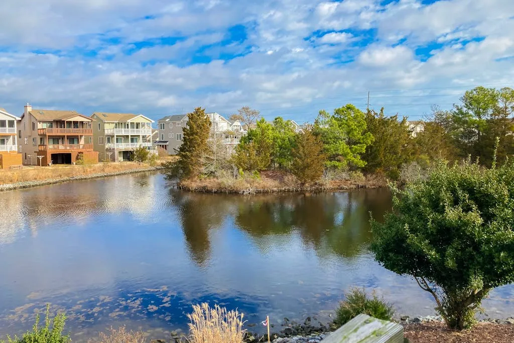 A pond bordered by trees and residential buildings beneath a partly cloudy sky.