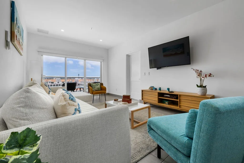 Settle into your bright, airy living space where coastal hues and modern comfort blend seamlessly. Floor-to-ceiling windows frame inviting views while plush seating beckons you to unwind after your beach day.