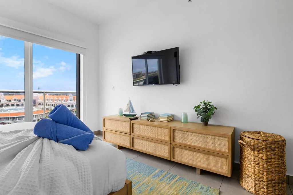 Your bright, airy bedroom features a wall-mounted TV, natural wood furnishings, and coastal decor. Enjoy views under sunny skies.