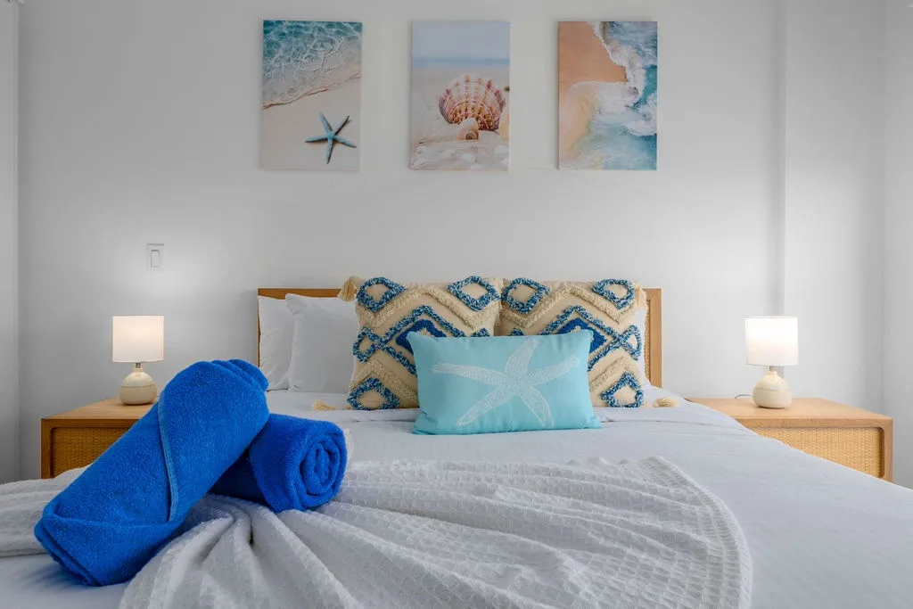 Sink into crisp linens and ocean-inspired hues, where coastal charm meets cozy comfort. Your restful retreat awaits with thoughtful touches and warm bedside lighting.
