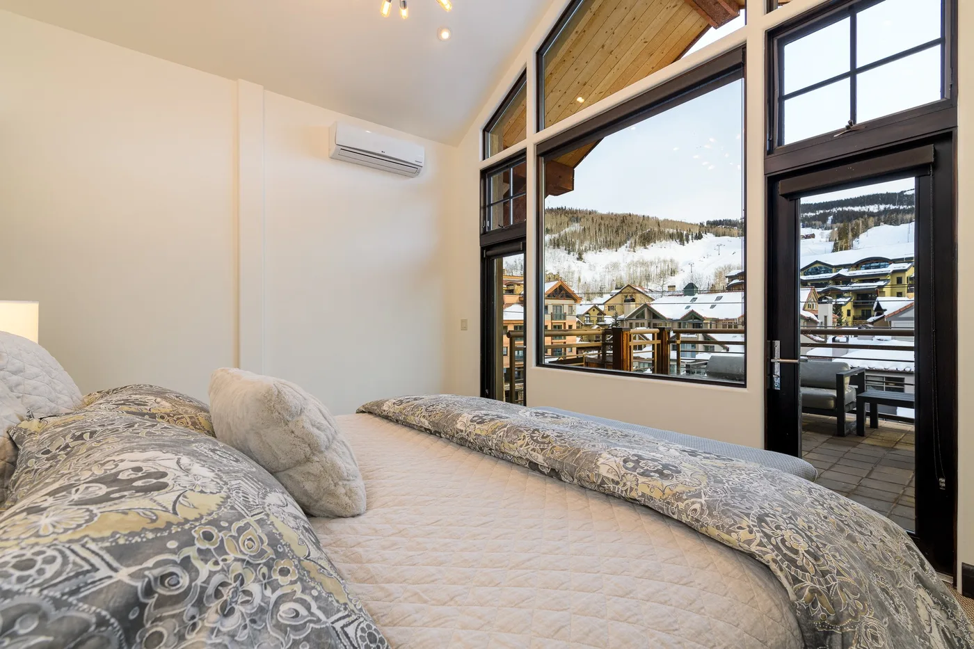 A bedroom with patterned bedding and large windows overlooking a snowy hillside.