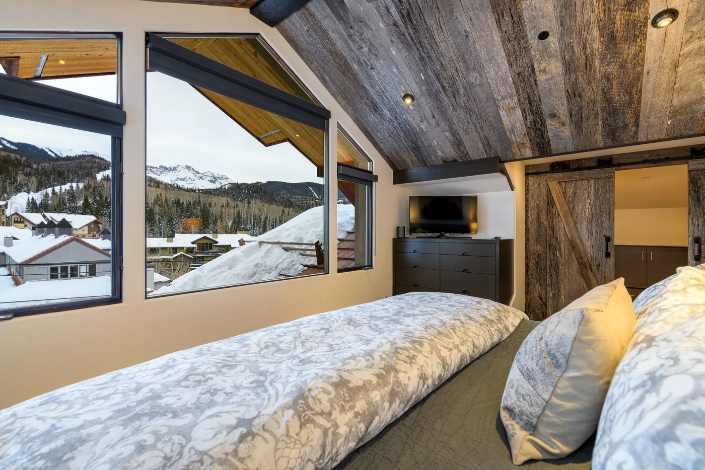A bedroom with two beds, large windows, and a television on a dresser.