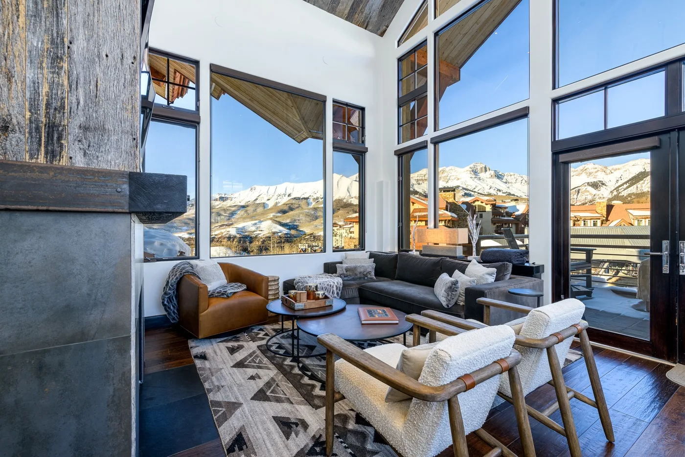 A living room with seating beside tall windows overlooking a snowy mountain landscape.
