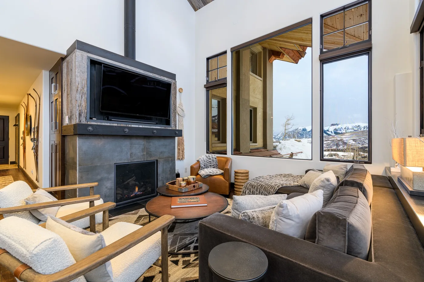 A living room with a stone fireplace, television, and seating beside large windows.