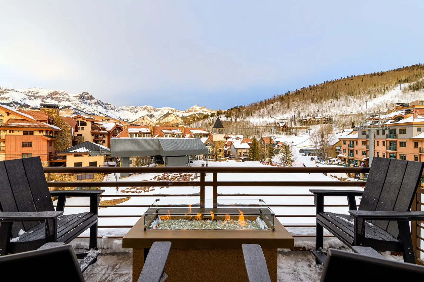 A balcony seating area overlooks a snow-covered mountain village.