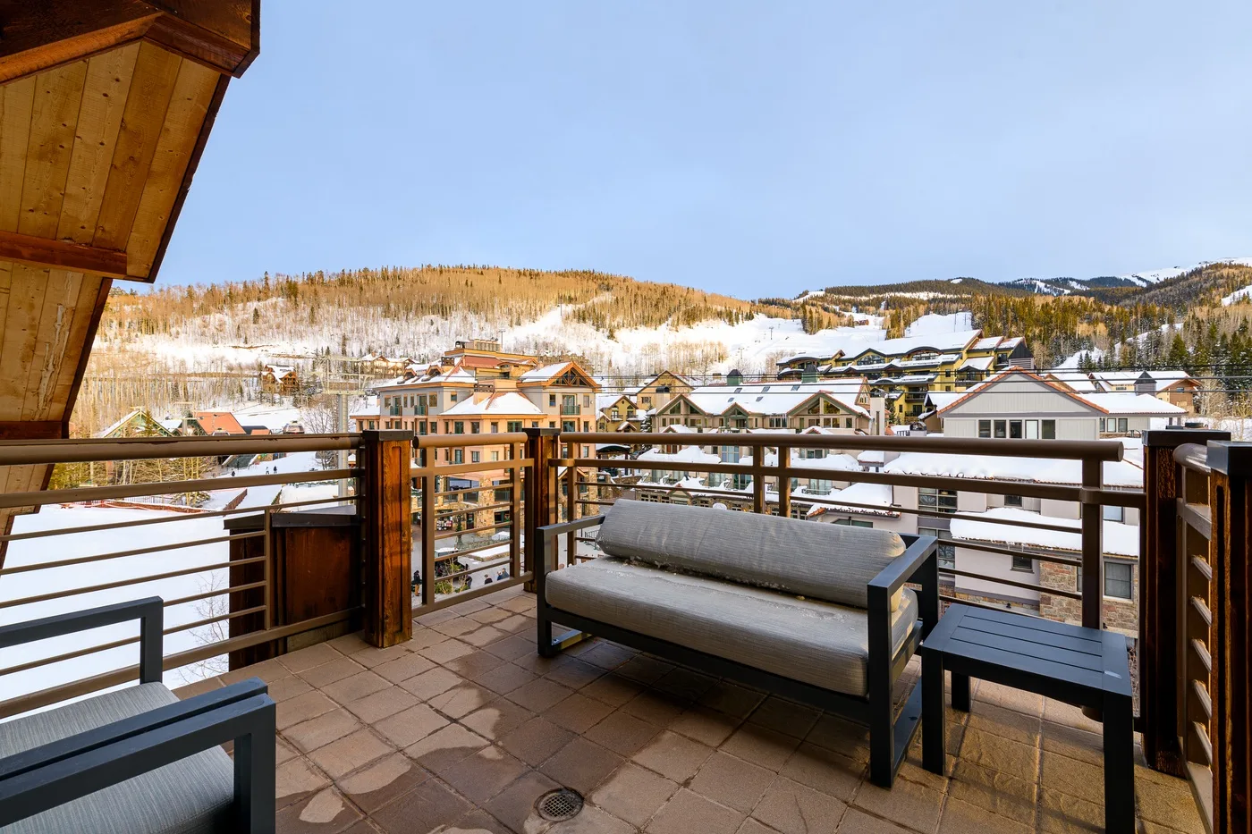 A balcony seating area overlooks snow-covered buildings and wooded hills.
