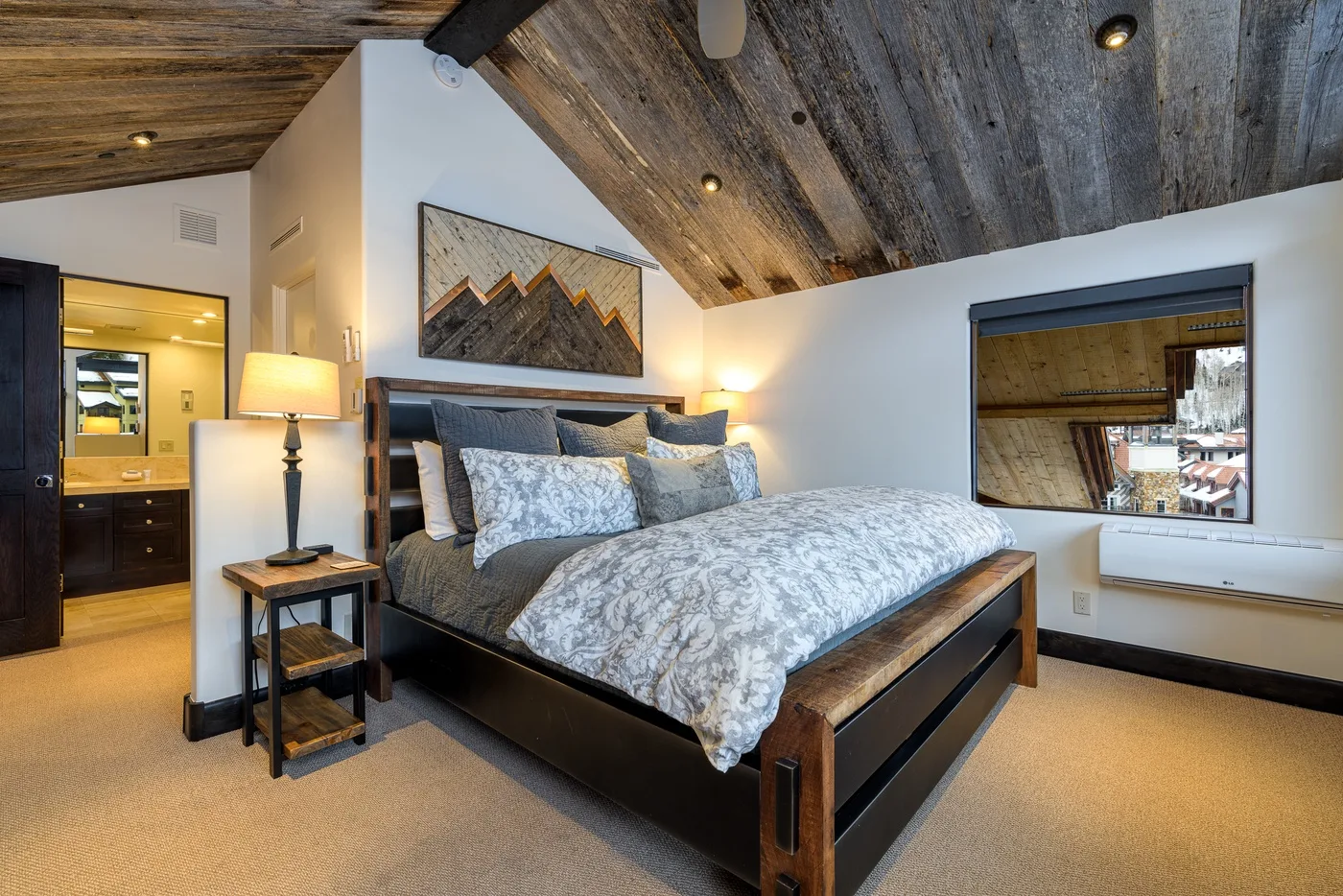 A bedroom with a large bed, bedside table, and sloped wood ceiling.