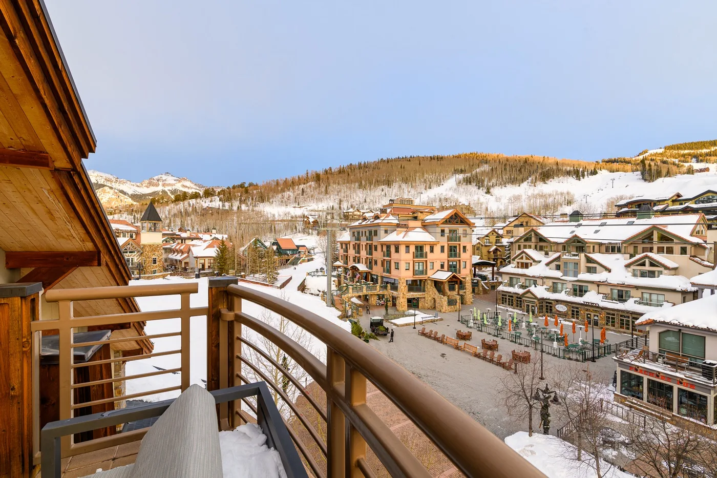 A wooden balcony overlooks snow-covered buildings and a hillside.