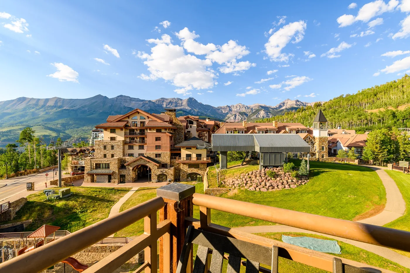 A mountain resort complex with stone buildings, green lawns, and surrounding peaks.