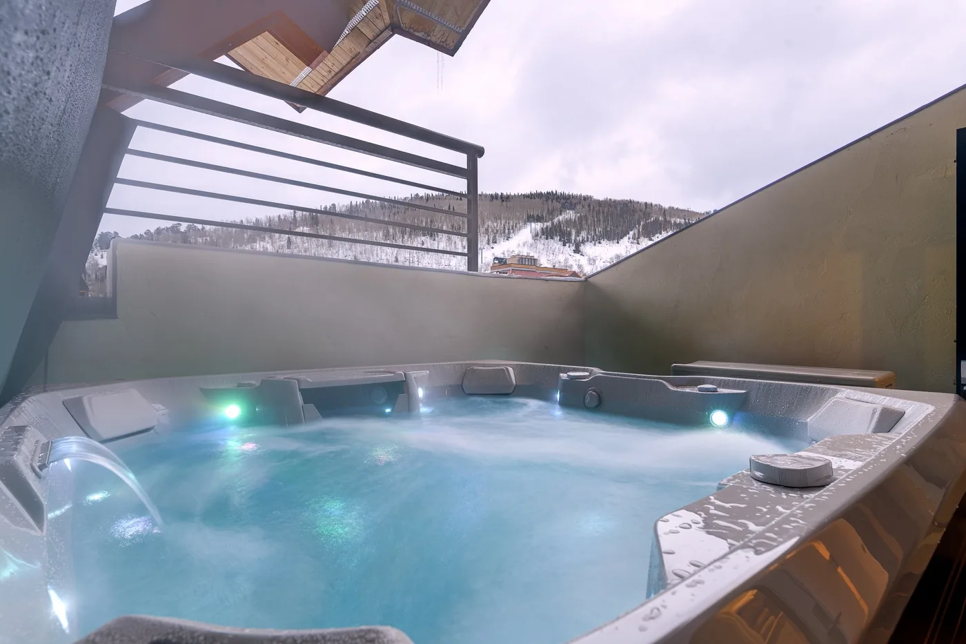 An outdoor hot tub sits on a terrace overlooking a snowy mountain landscape.
