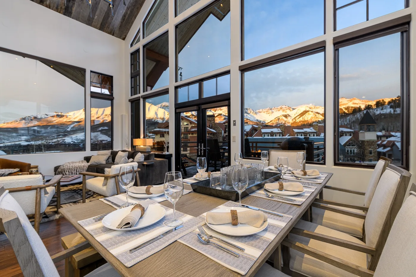 A dining area with set tables and floor-to-ceiling windows overlooking snowy mountains.