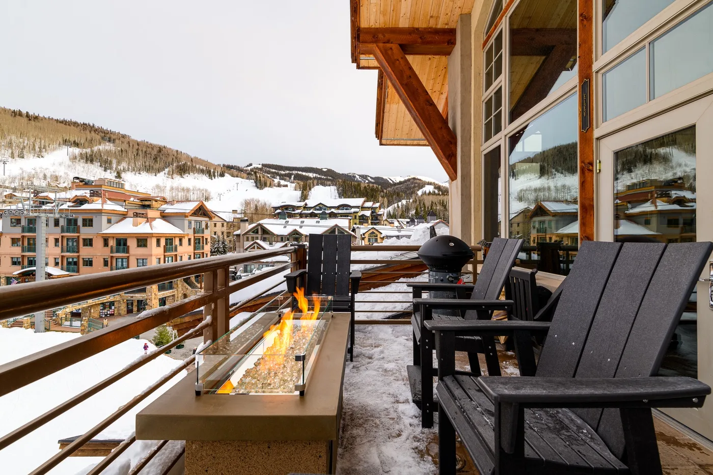 A snowy outdoor deck with seating overlooks a mountain village.