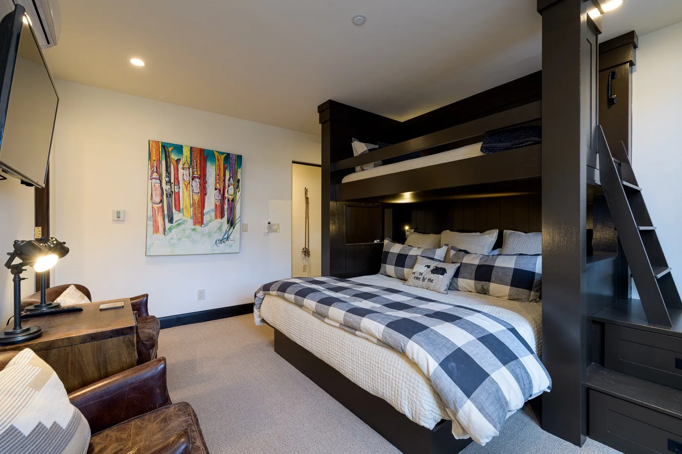 A bedroom with a large bed beneath a dark built-in bunk structure.