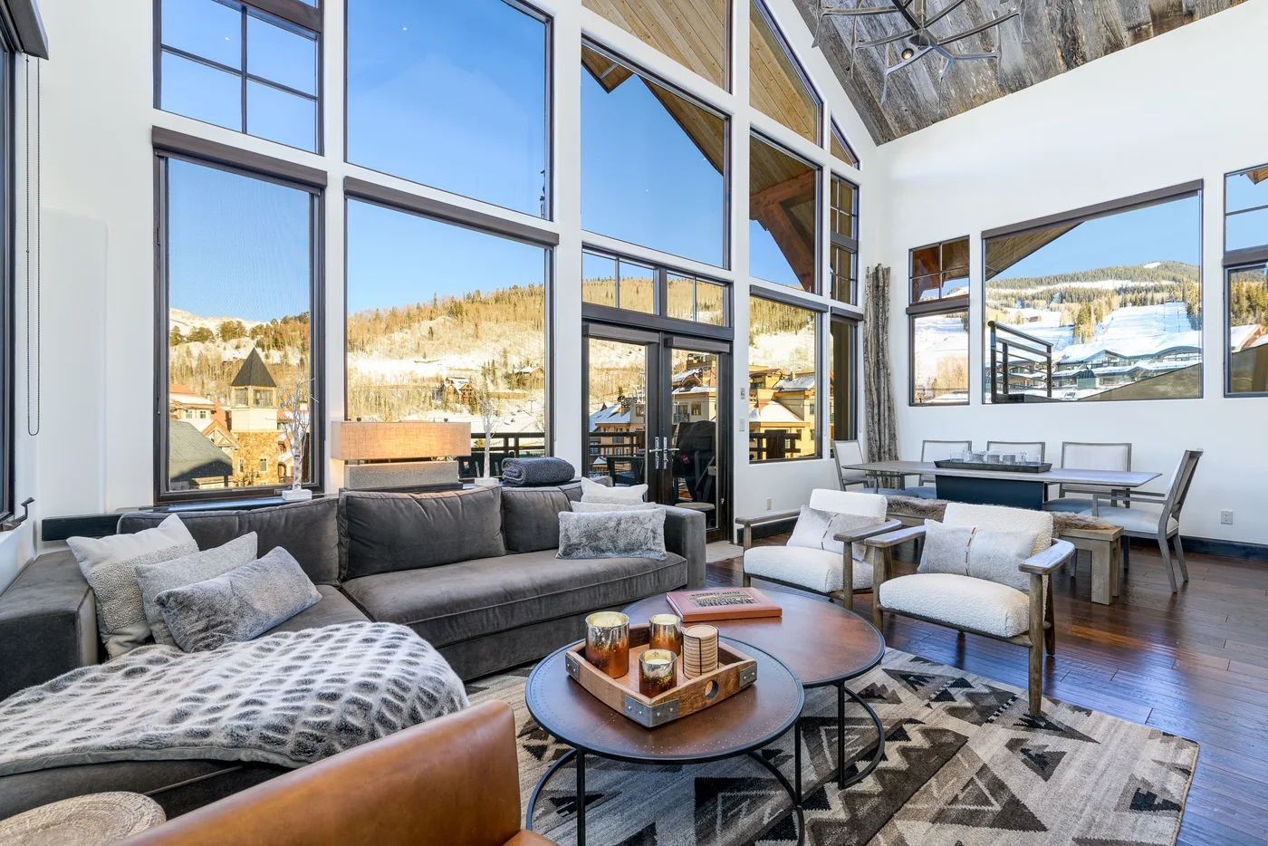 A bright living room with tall windows, seating, and a view of the snowy hills.