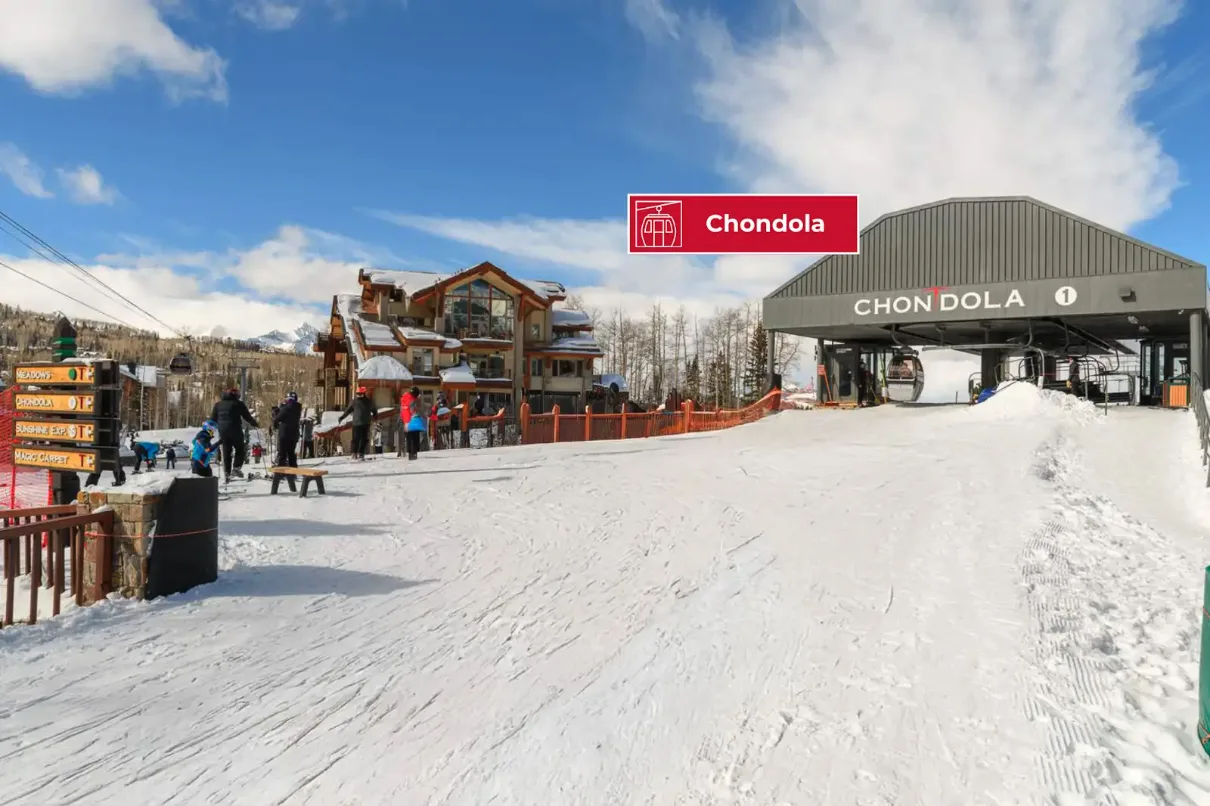 A snowy ski area entrance with a large covered structure and nearby buildings.