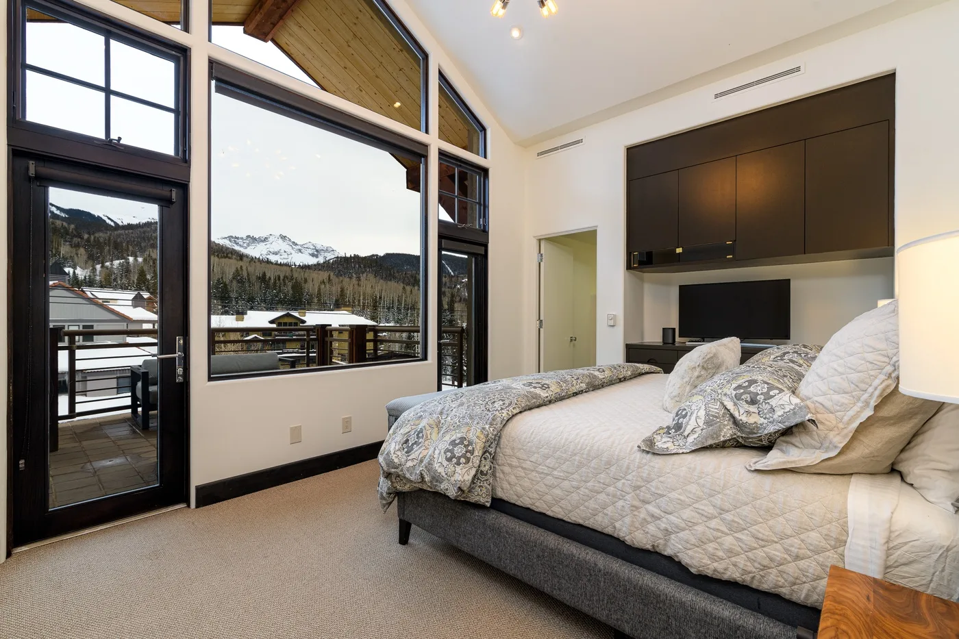 A bedroom with a bed beside large windows overlooking a snowy mountain landscape.