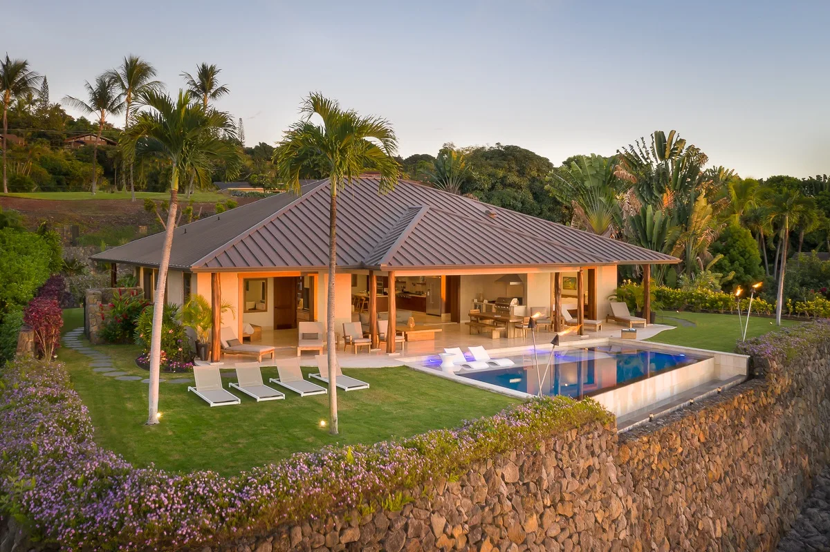 Una casa moderna se abre a un césped y una piscina, rodeada de plantas tropicales.