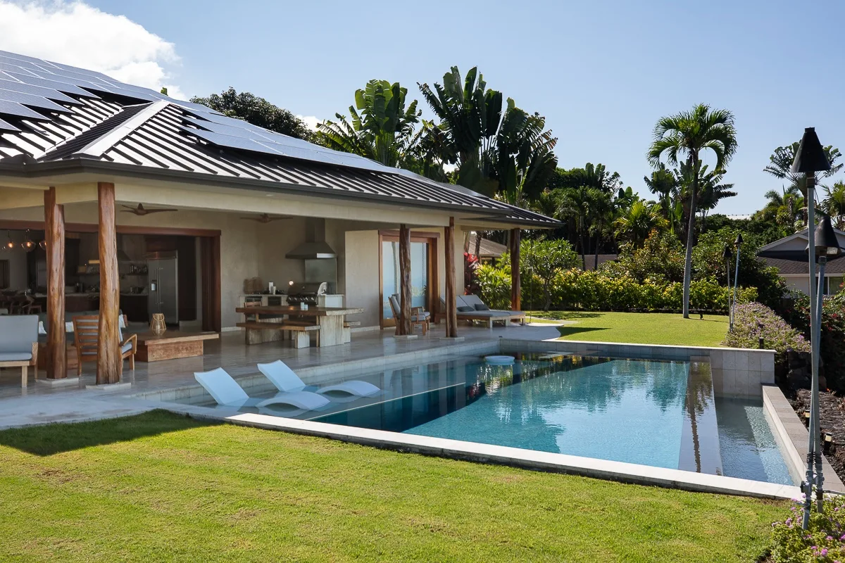 Una casa moderna se abre a una piscina, con vegetación de jardín al fondo.