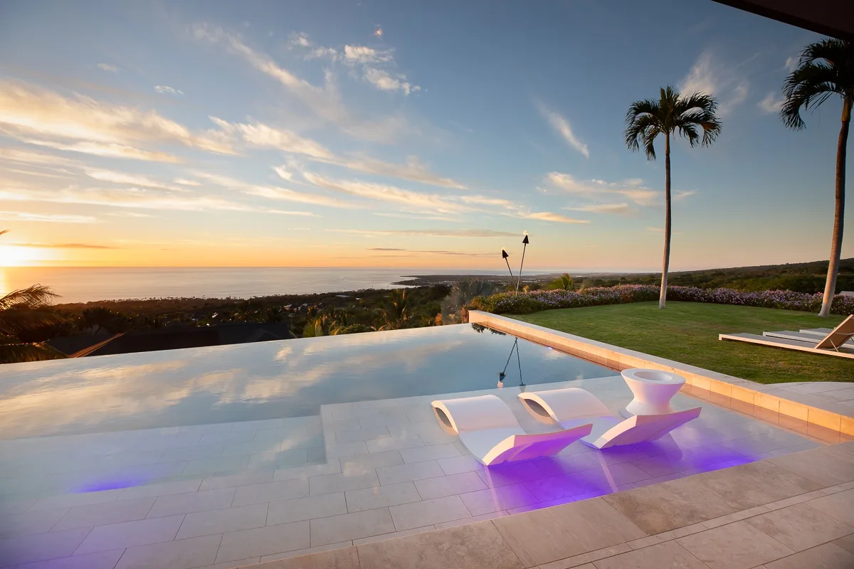 Una piscina infinita mira al océano al atardecer, con tumbonas junto al agua.