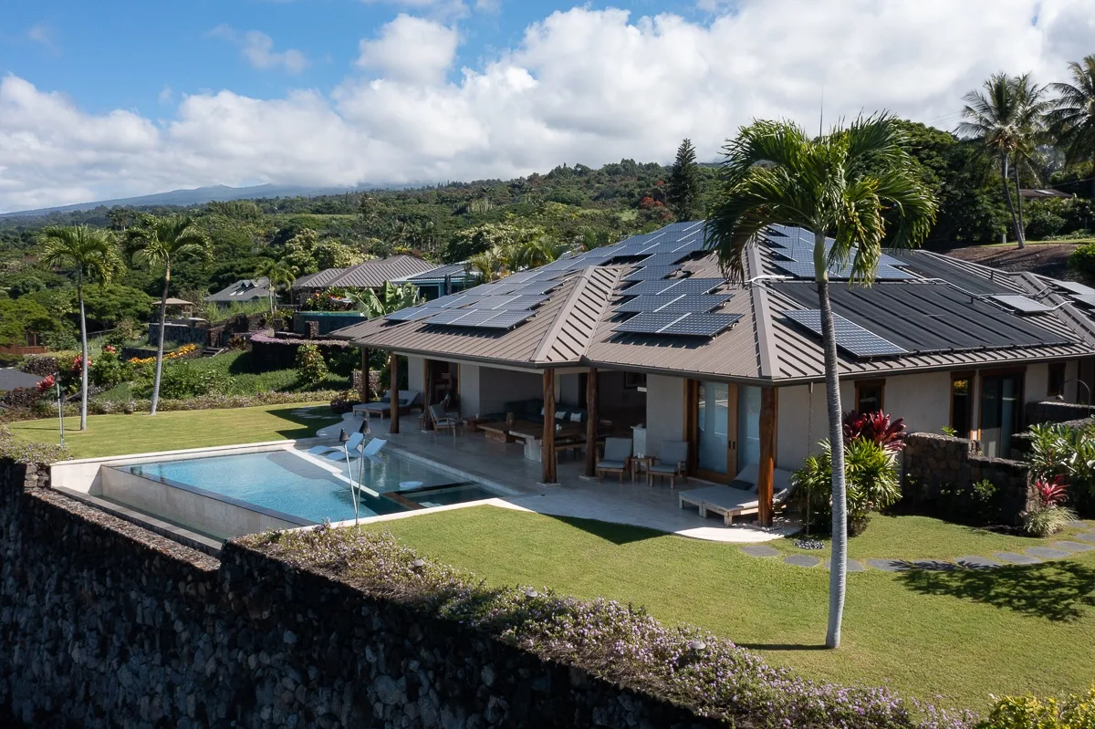 Un edificio bajo con paneles solares está junto a una piscina y jardines.