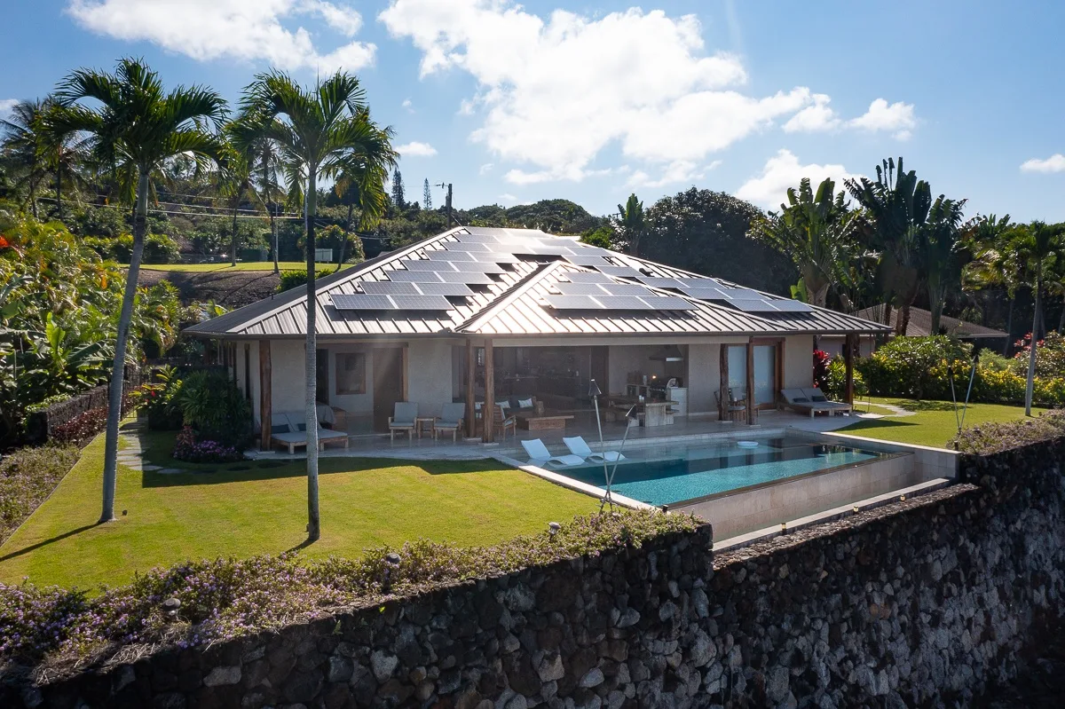 Una casa moderna está junto a una piscina, con césped y plantas tropicales.