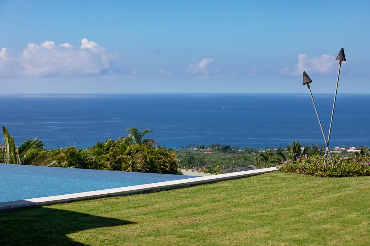 Un césped y una piscina ofrecen vistas al océano bajo un cielo despejado.