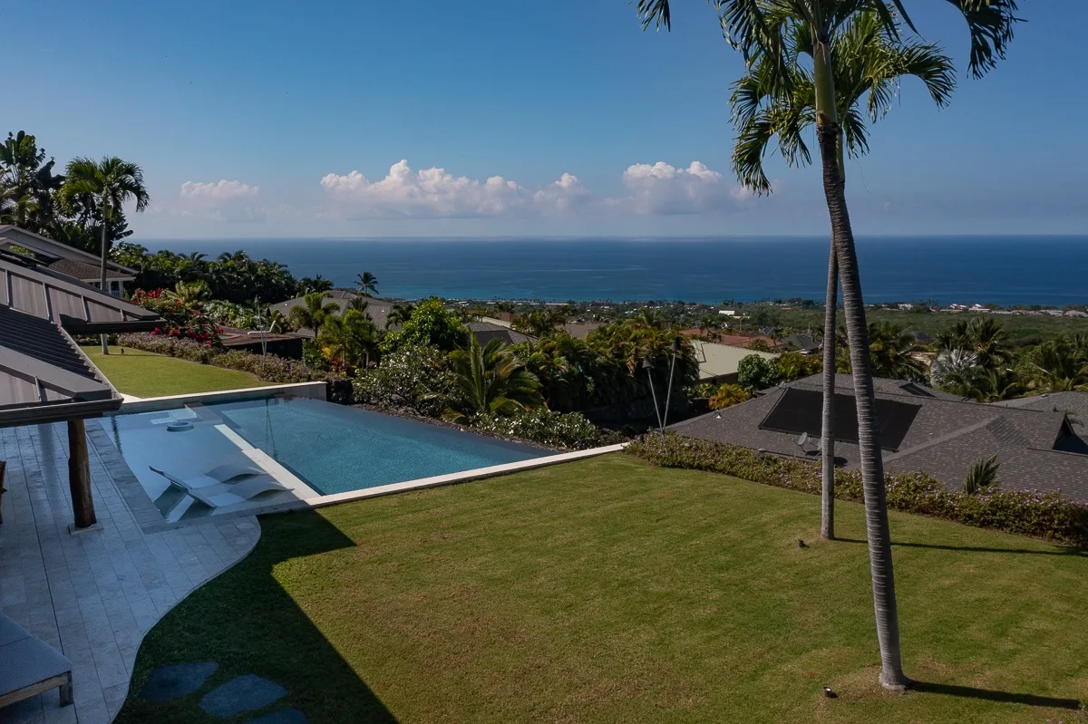 Una piscina y un césped ofrecen vistas al océano bajo un cielo azul despejado.