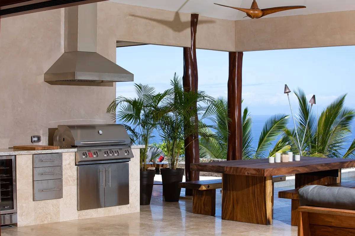 Una cocina y comedor al aire libre con parrilla empotrada y mesa de madera.