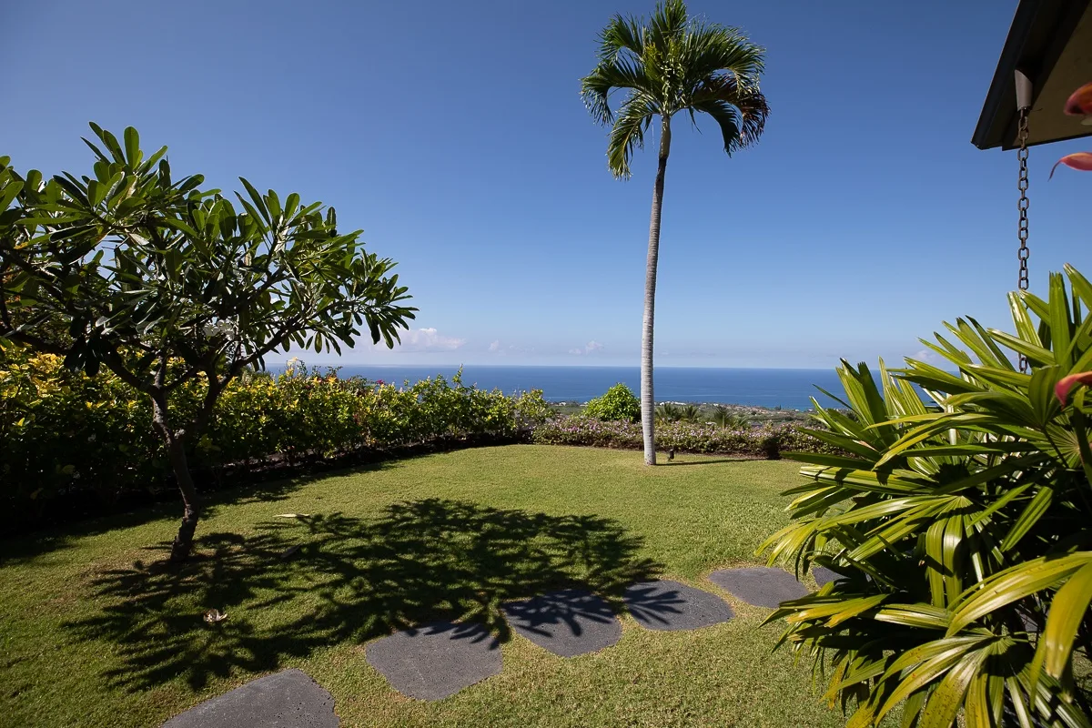 Un jardín soleado con césped, palmeras y vistas al océano.