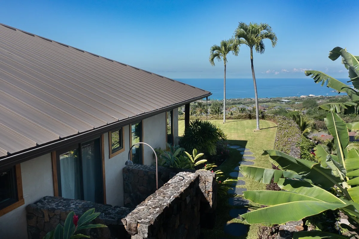 Una casa costera mira al océano, con palmeras y plantas tropicales en el jardín.
