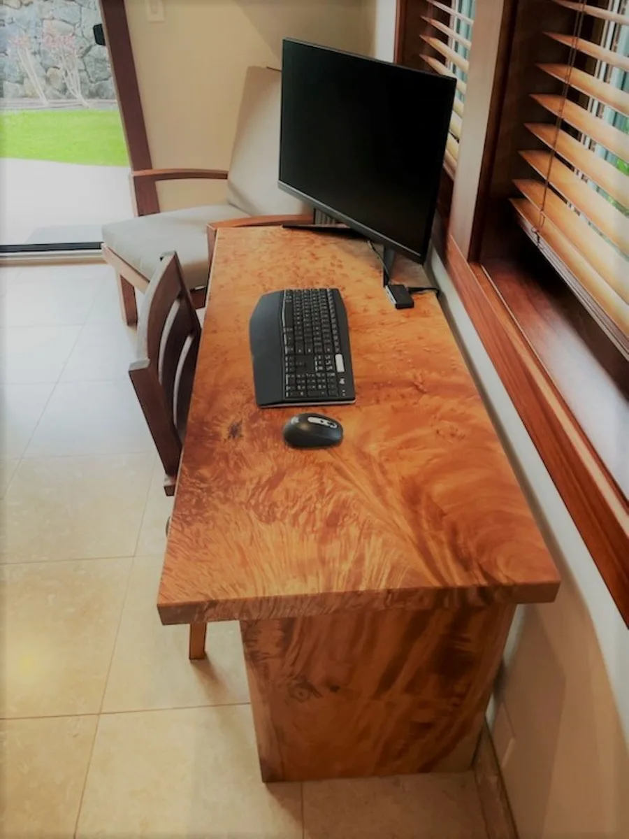 Un escritorio de madera con monitor y teclado está junto a una ventana.