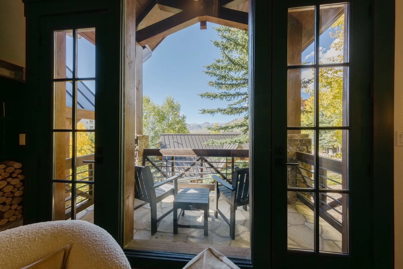 A bright dining area opens onto a deck with outdoor seating and leafy trees.