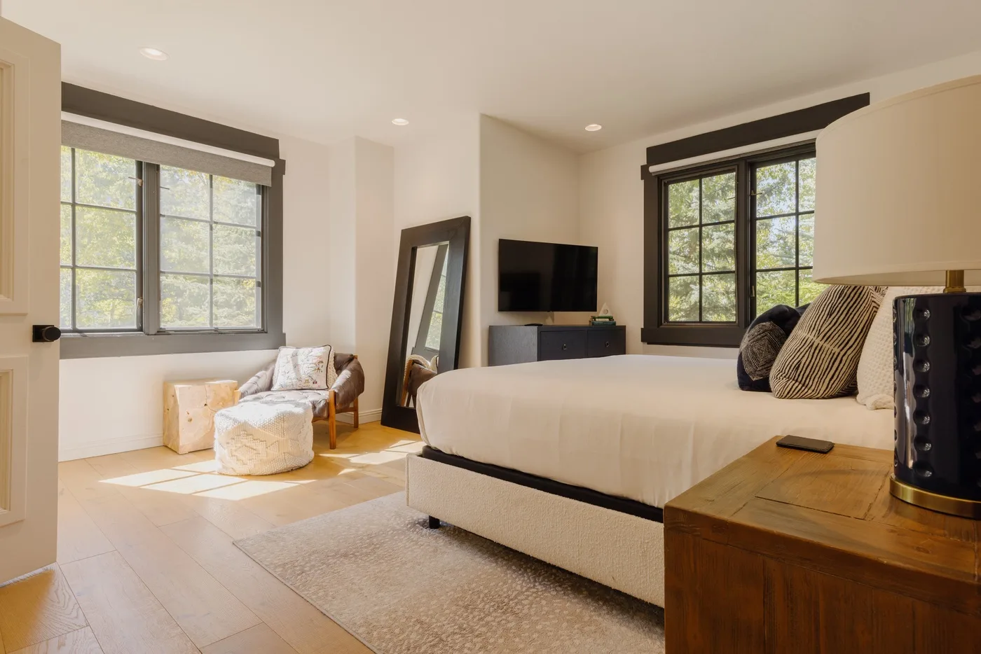 A bright bedroom with a large bed, two windows, and a television.