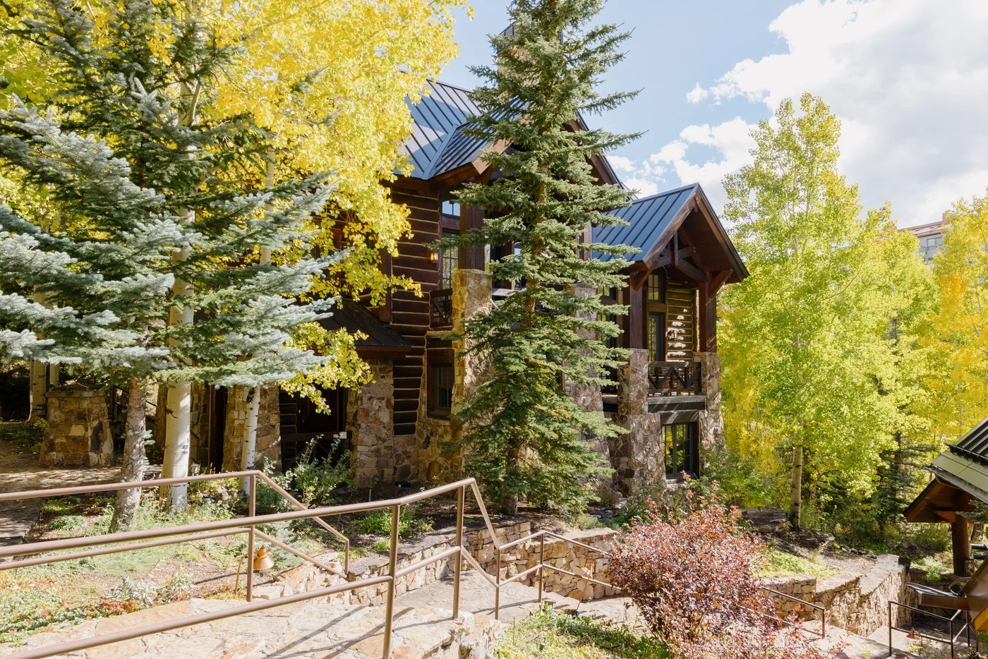 A stone lodge stands among evergreen and yellow-leaved trees.