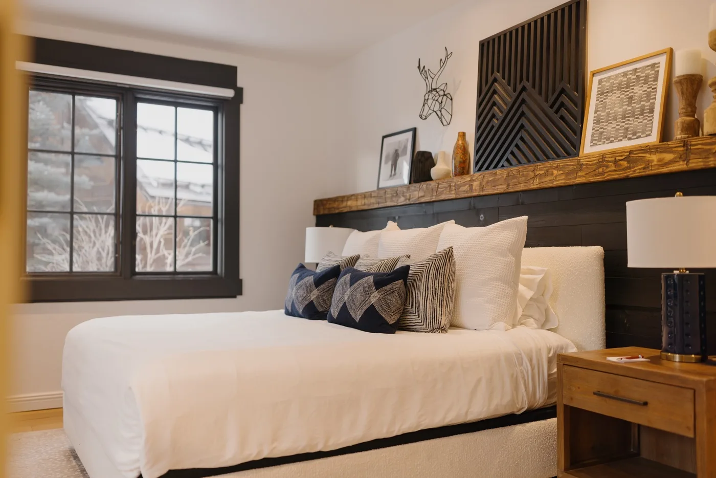 A bedroom with a neatly made bed and a dark-framed window.