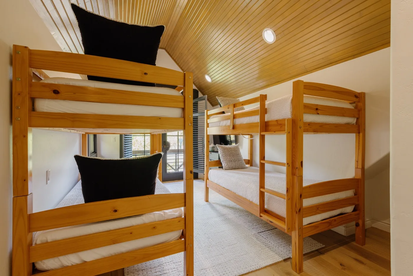 A bunk bedroom with wooden bunk beds and a sloped wood ceiling.