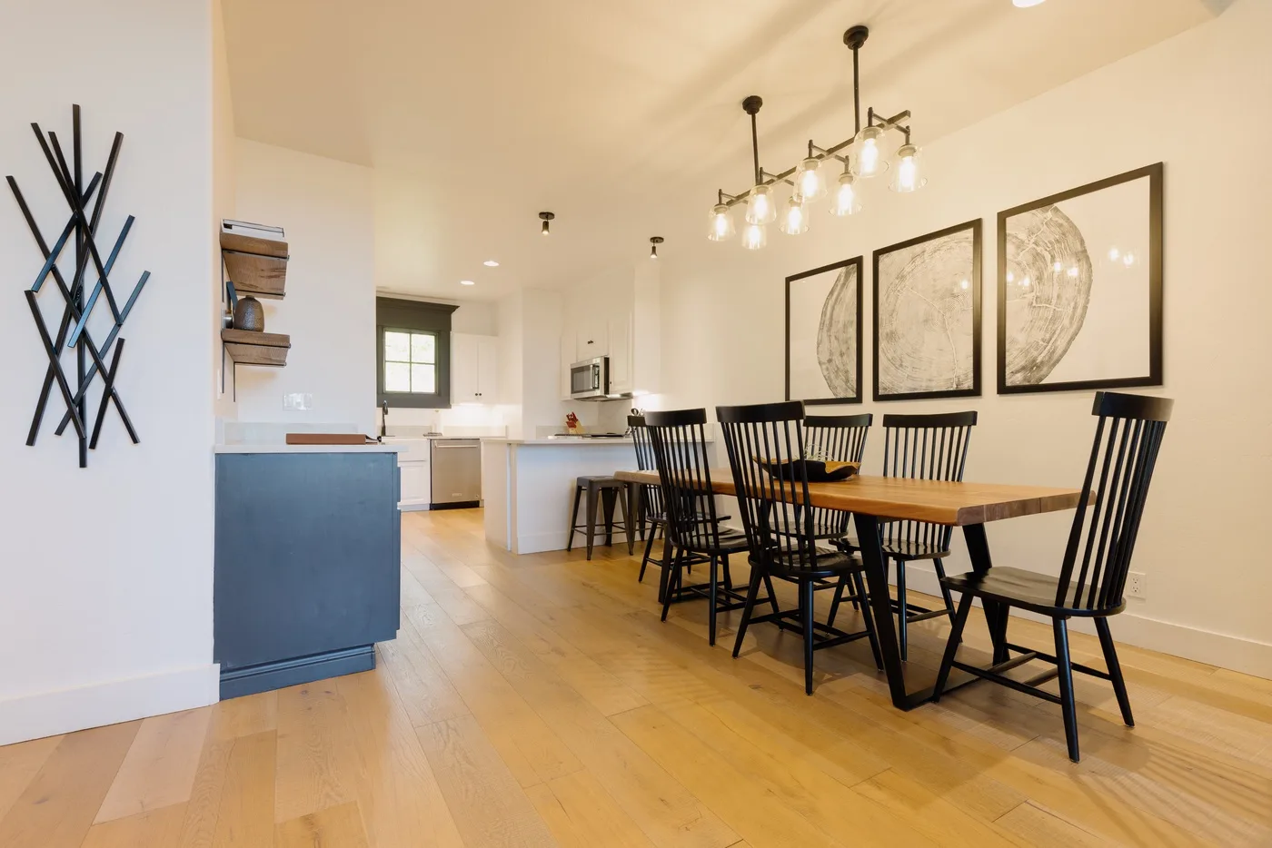 Dining area with a long table and black chairs beside an open kitchen.