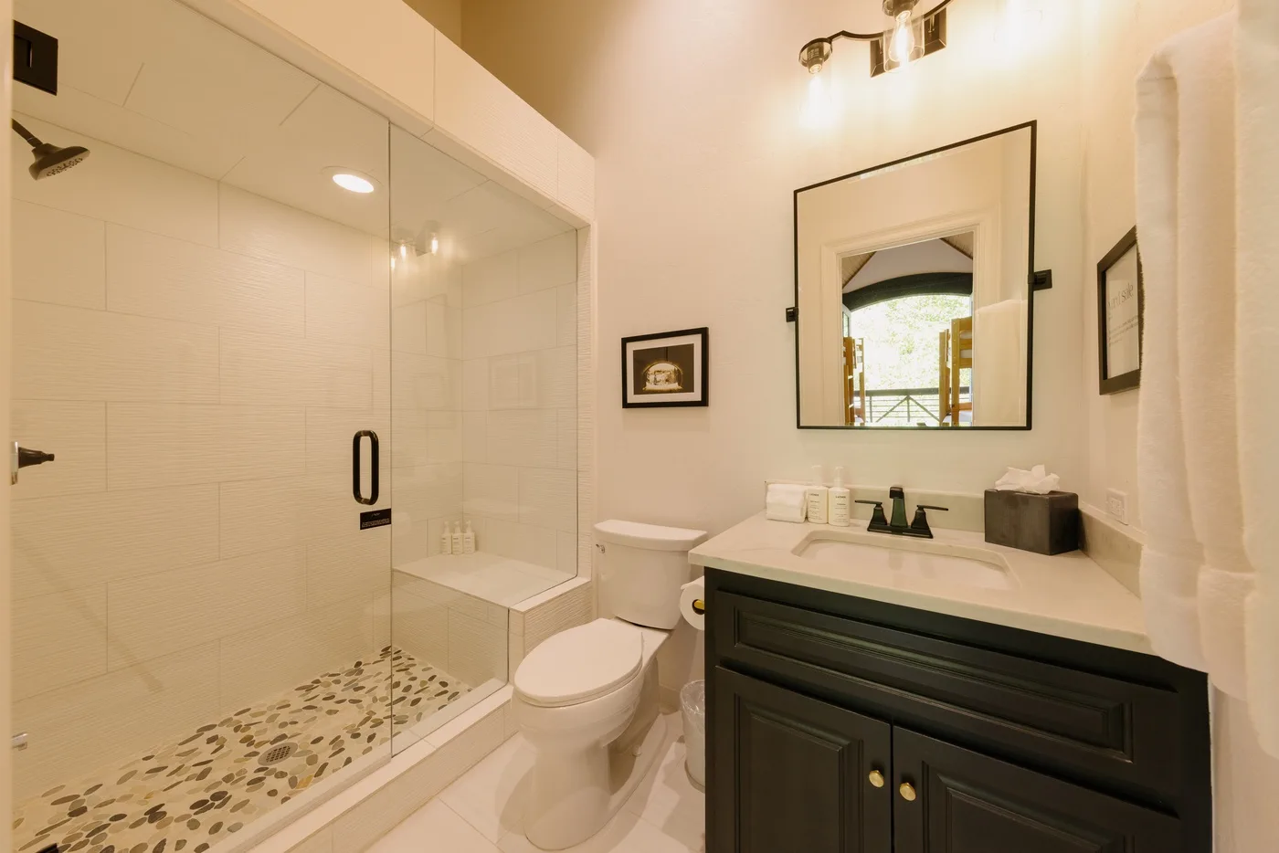 A bright bathroom with a glass shower, toilet, and dark vanity.