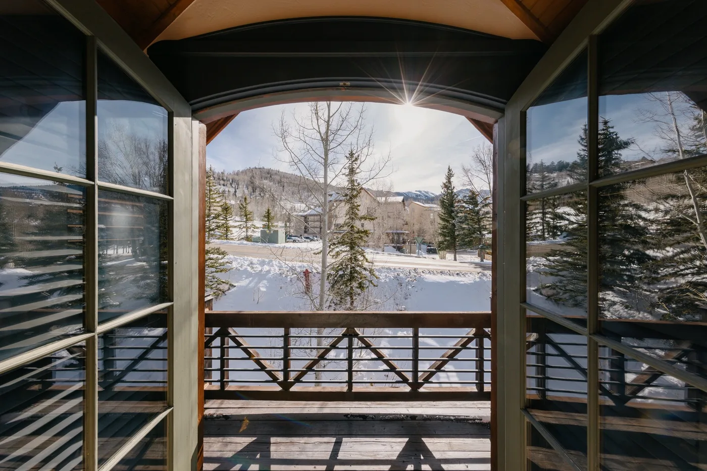 A covered balcony overlooks a snow-covered landscape with trees and distant hills.