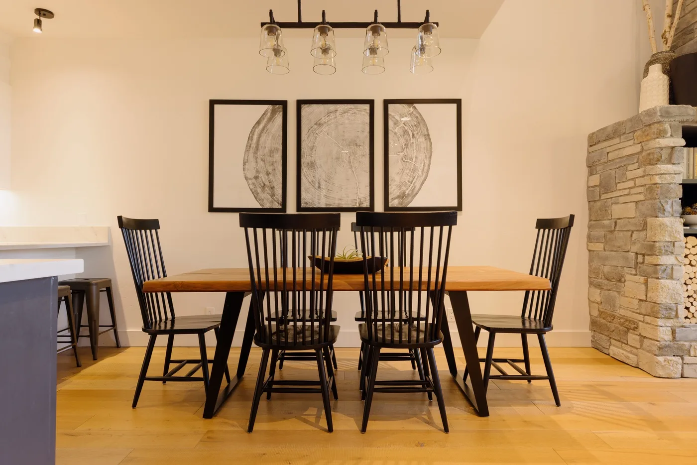 A dining room with a wooden table and black chairs beneath framed artwork.