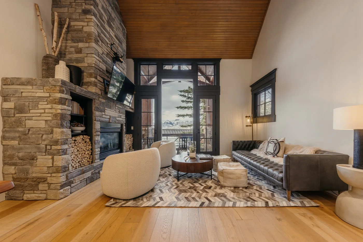 A living room with a stone fireplace, seating, and tall windows opening onto a balcony.