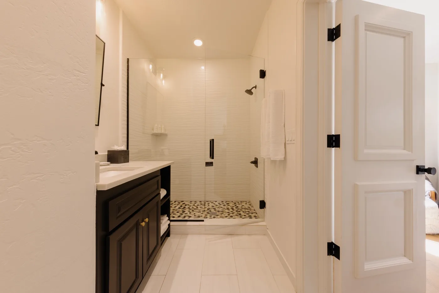 A bright bathroom with a walk-in shower and a dark vanity.