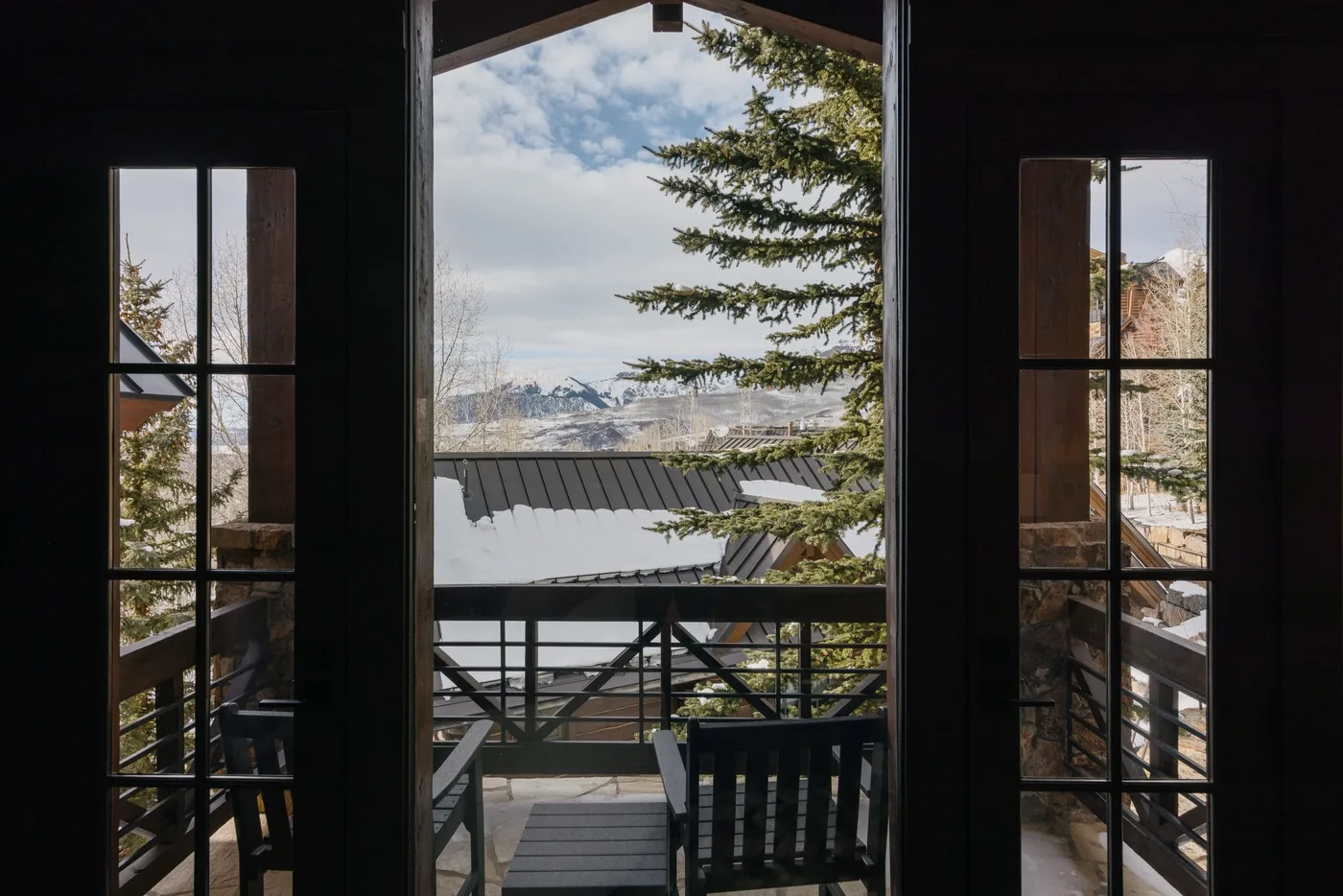 A dark interior doorway opens onto a balcony overlooking a snowy mountain landscape.