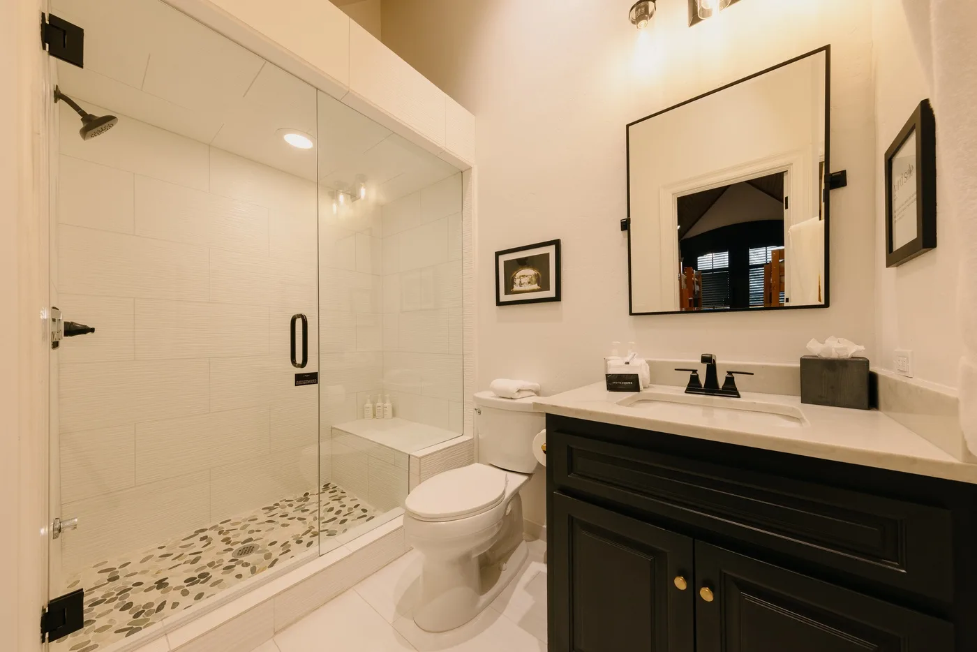 A bright bathroom with a glass shower, toilet, and dark vanity.