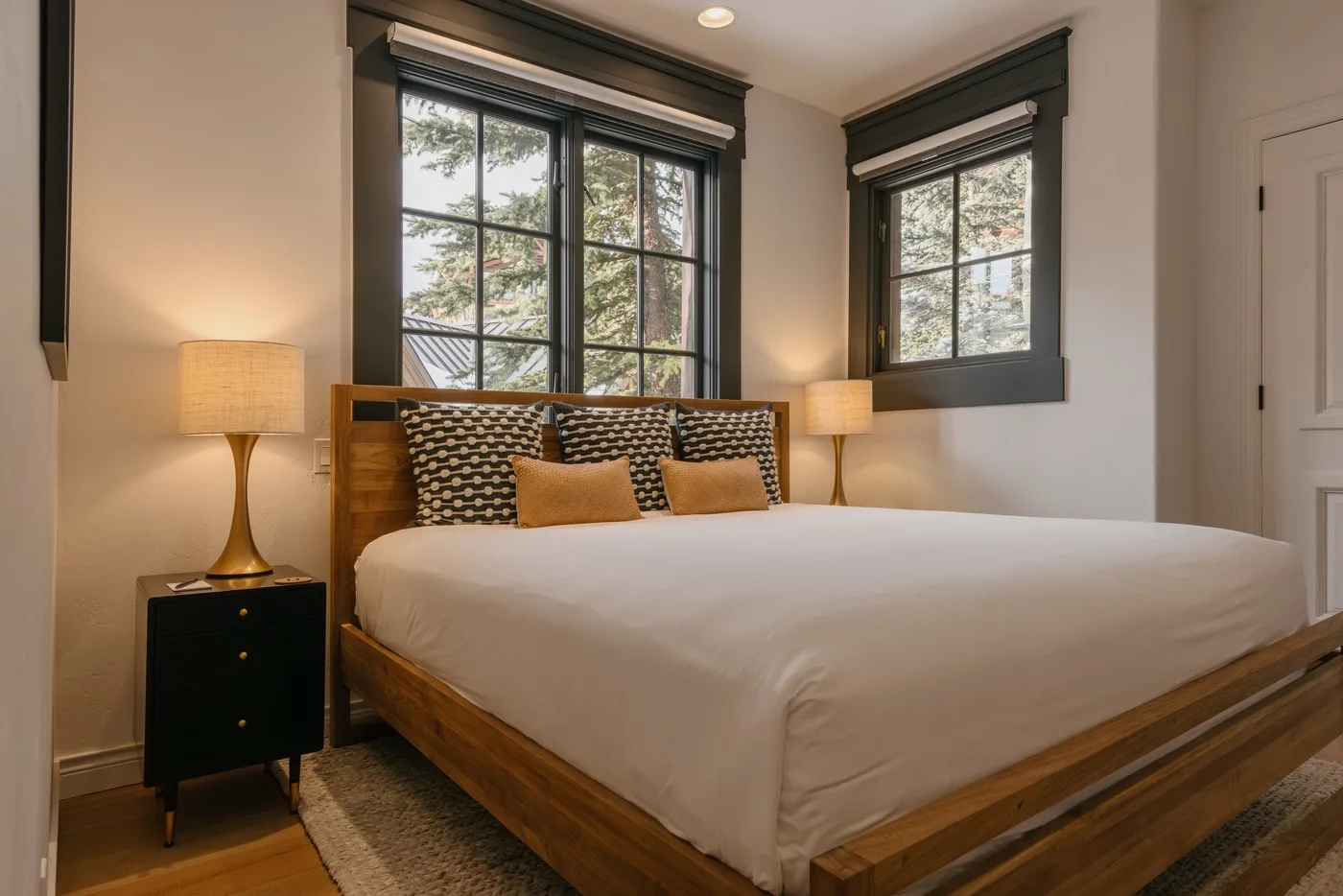 A bedroom with a large bed and two windows overlooking trees.
